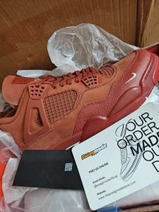 A rust-red suede high-top sneaker photographed in its delivery box