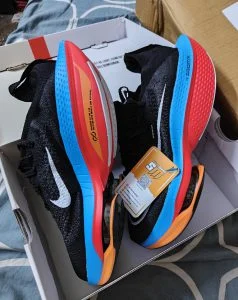 Black running shoes with red and blue soles, unboxed