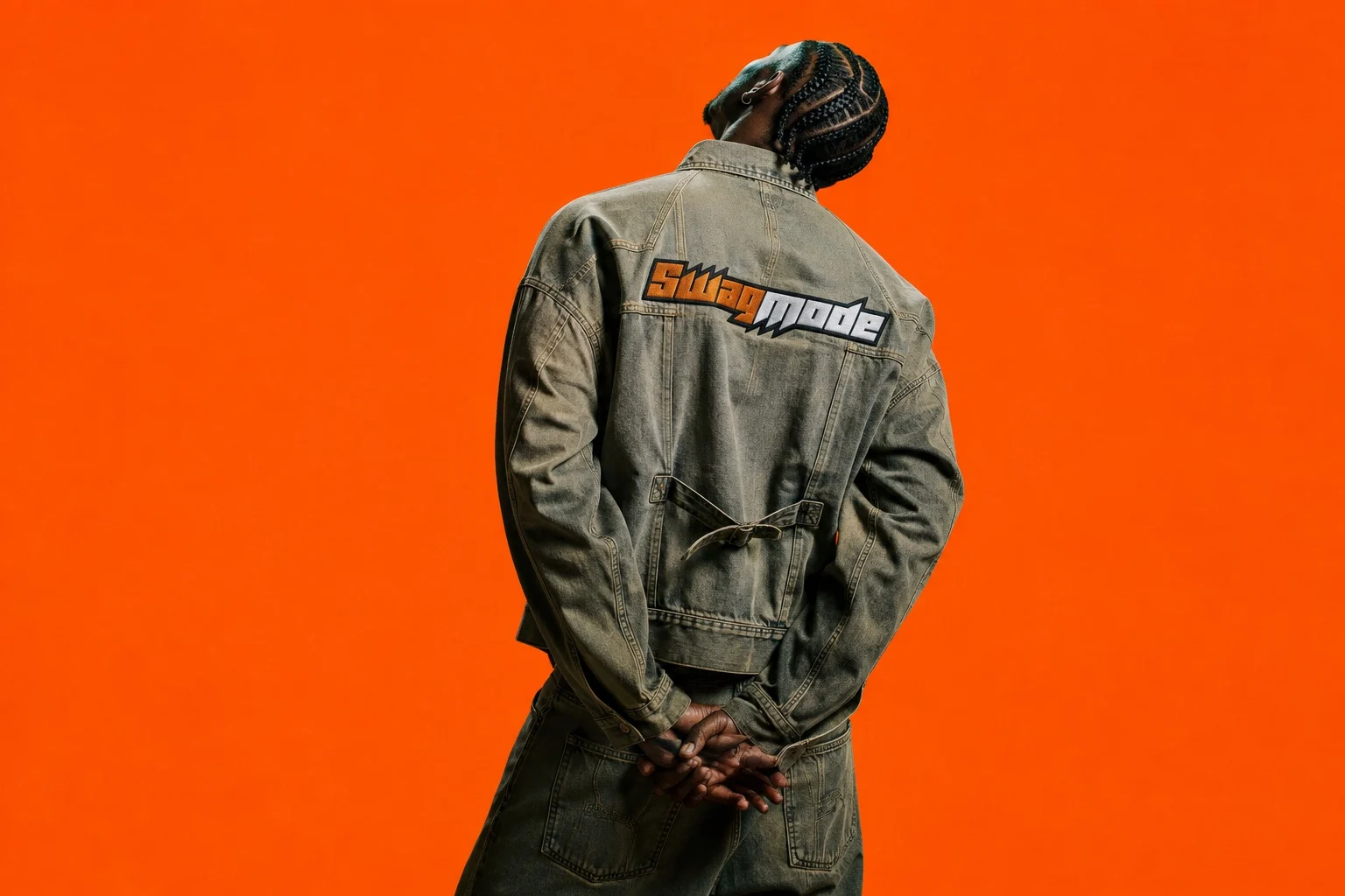 A model seen from behind wearing a washed denim jacket with the Swag Mode logo across the back, against a solid orange background