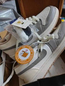 A pair of cream and grey low-top sneakers in their box with the Swag Mode hang tag, photographed by the customer who received them