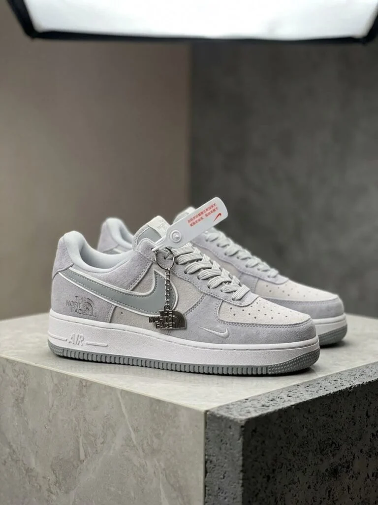Grey and white low-top suede sneaker with a metal charm on the laces